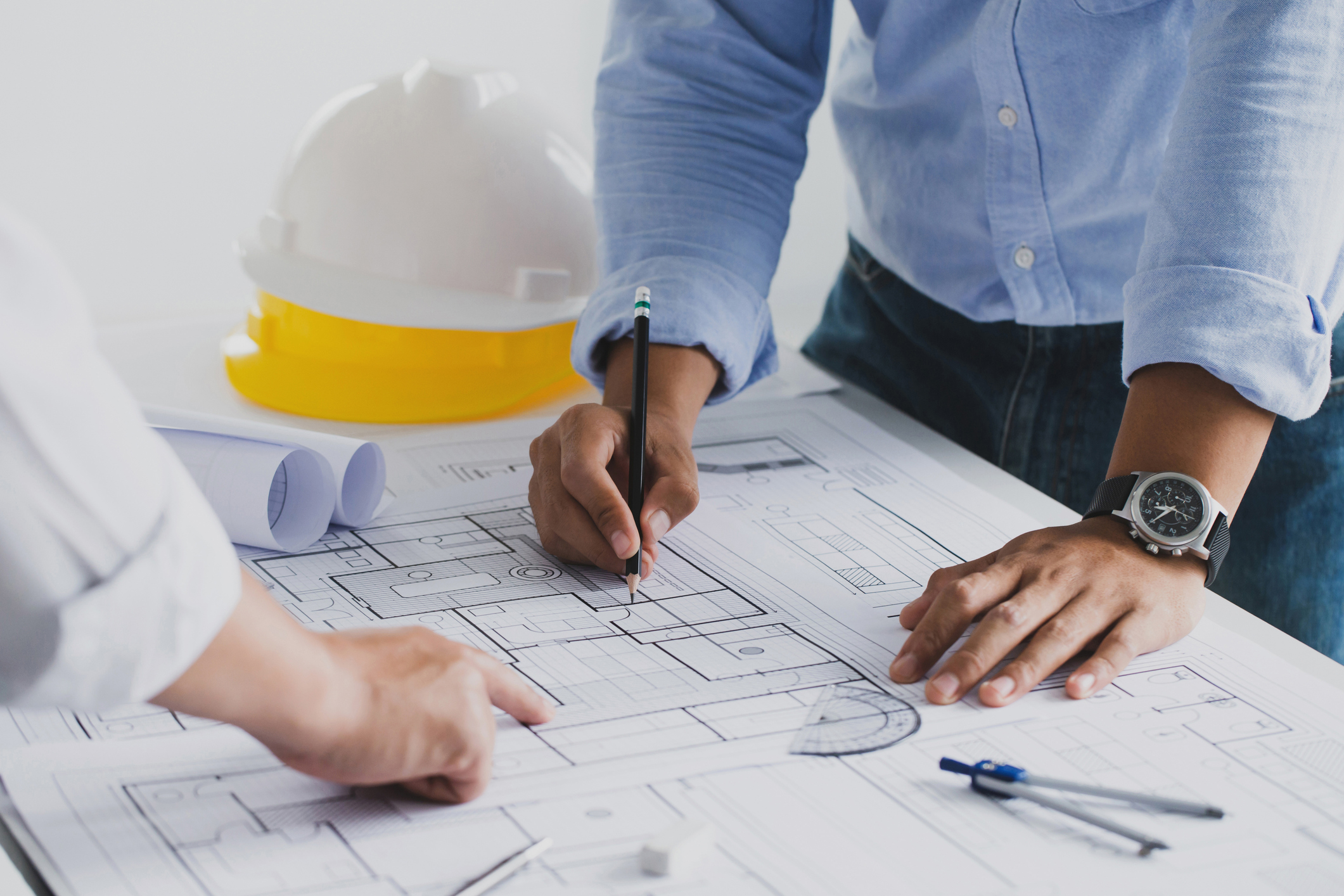 Two professionals reviewing architectural blueprints with safety helmets in the background.