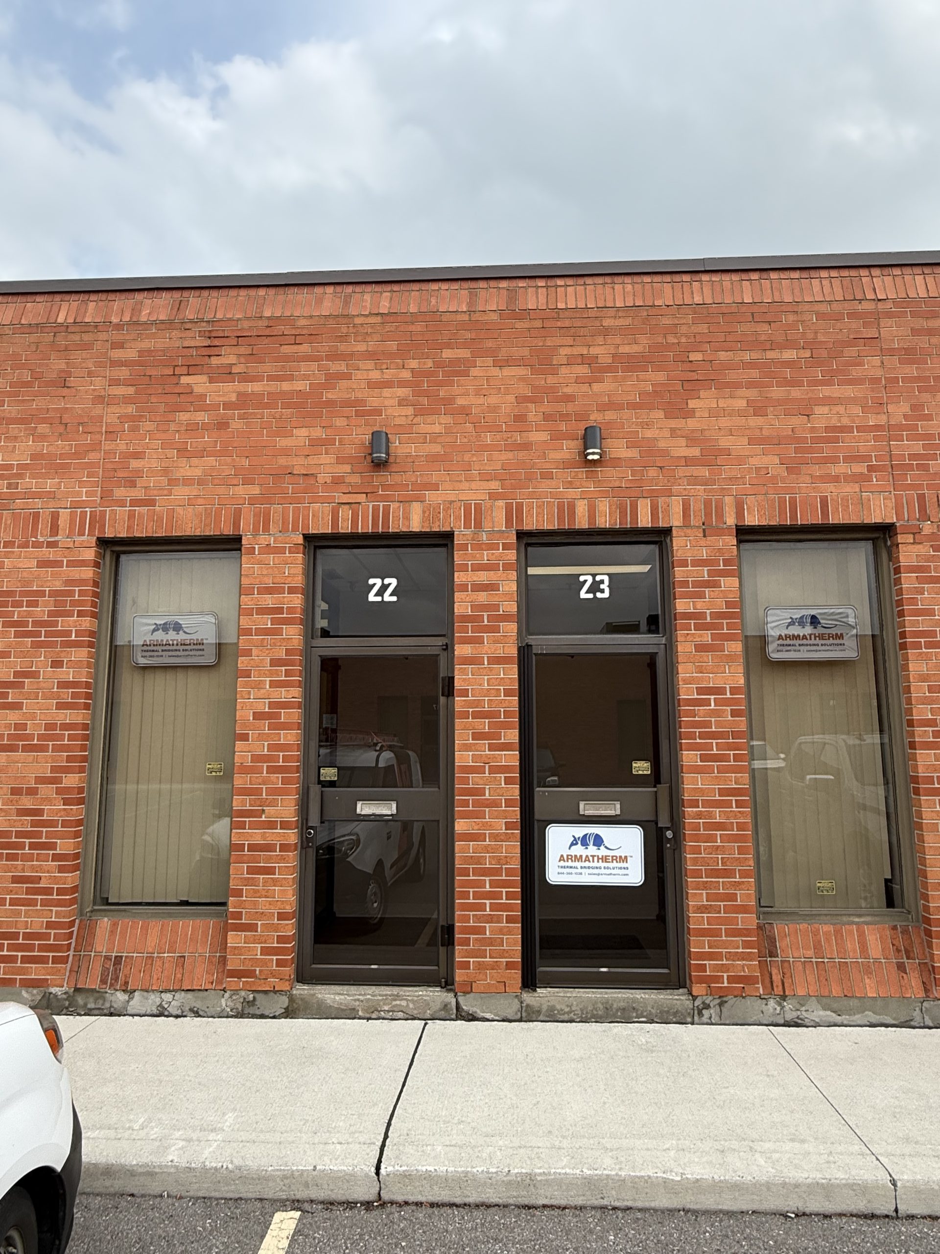 Exterior view of Armatherm’s new Canadian office entrance at units 22 and 23, with clear signage on glass doors and red brick facade.