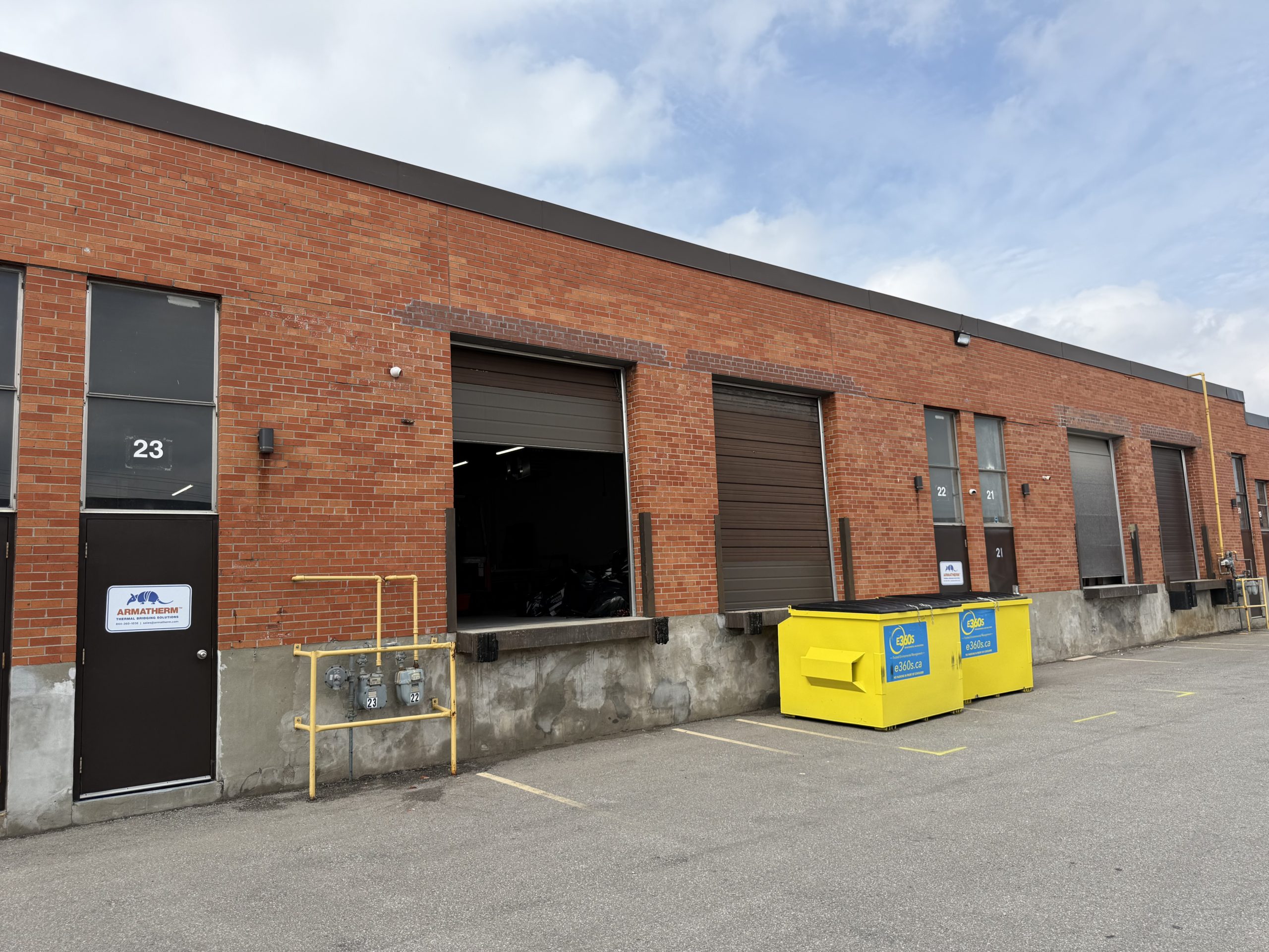 Back view of the Armatherm Canada facility showing unit 23 door, multiple loading docks, utility connections, and bright yellow waste bins.