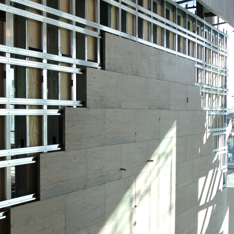 Interior installation of lightweight stone panels over an exposed aluminum cladding support frame on a commercial building wall.