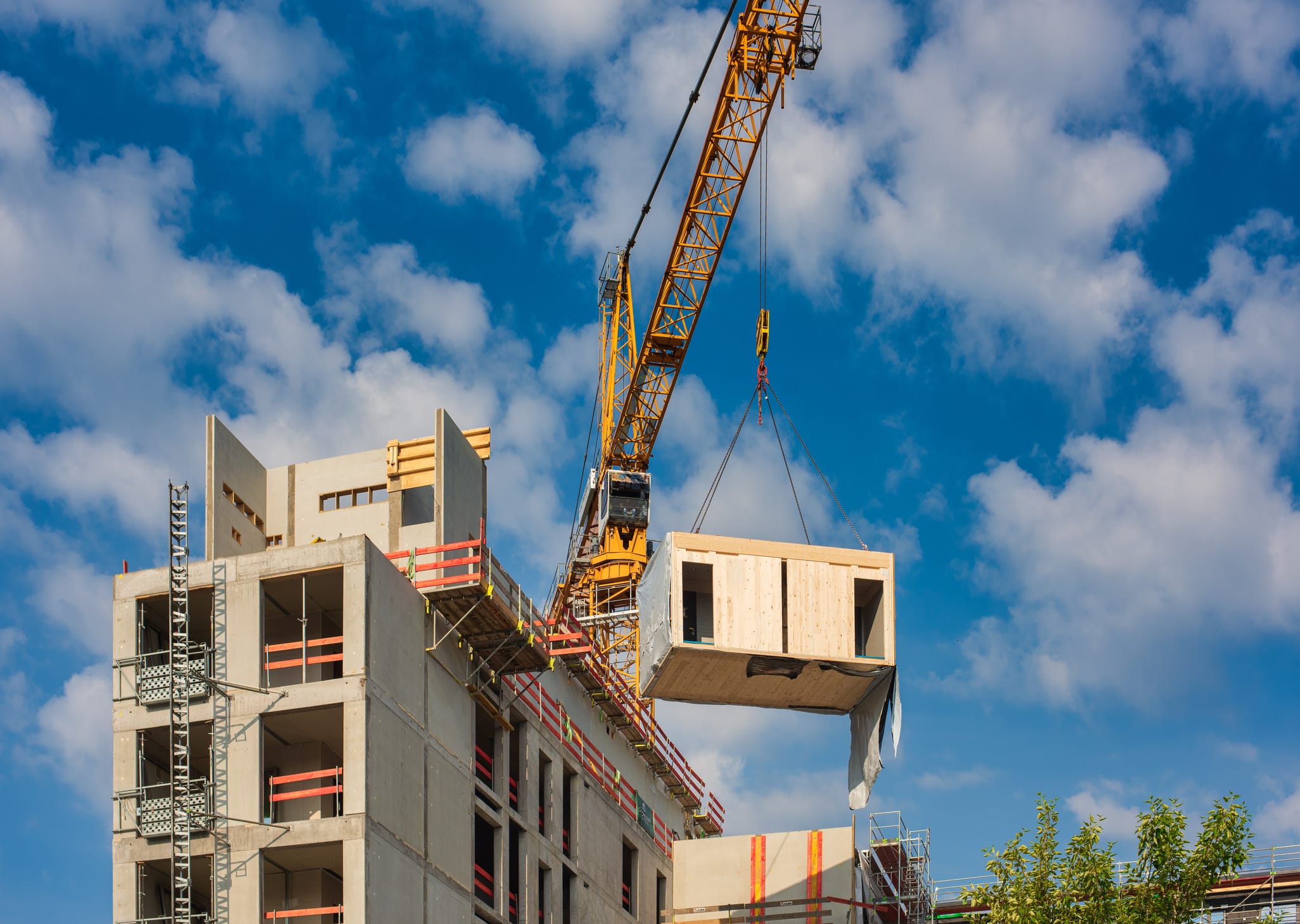 Crane positioning a timber modular unit onto a high rise concrete structure, showing the installation process used in energy efficient modular building construction
